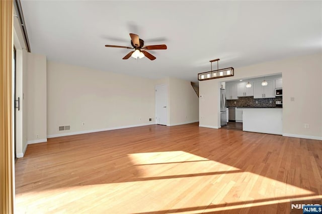 unfurnished living room featuring ceiling fan, light wood-style flooring, visible vents, and baseboards