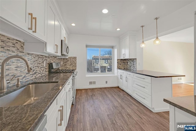 kitchen with light wood-style flooring, appliances with stainless steel finishes, hanging light fixtures, white cabinetry, and a sink