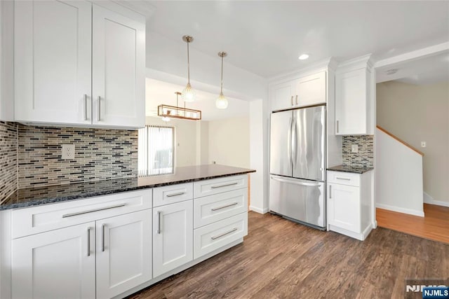 kitchen featuring freestanding refrigerator, white cabinets, decorative light fixtures, and dark stone countertops