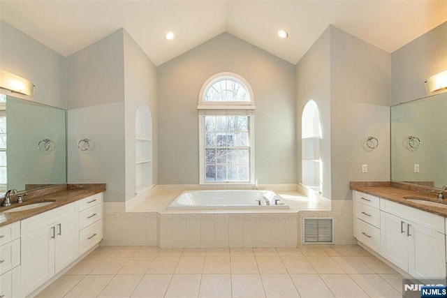 bathroom with tiled tub, vanity, tile patterned floors, and lofted ceiling