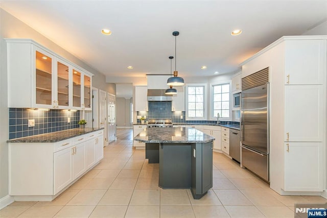 kitchen featuring built in appliances, white cabinetry, pendant lighting, a kitchen island, and dark stone counters