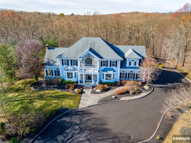 view of front facade featuring a chimney, a front lawn, a wooded view, and aphalt driveway