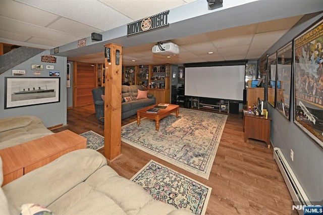 cinema room with a baseboard radiator, a drop ceiling, and wood finished floors