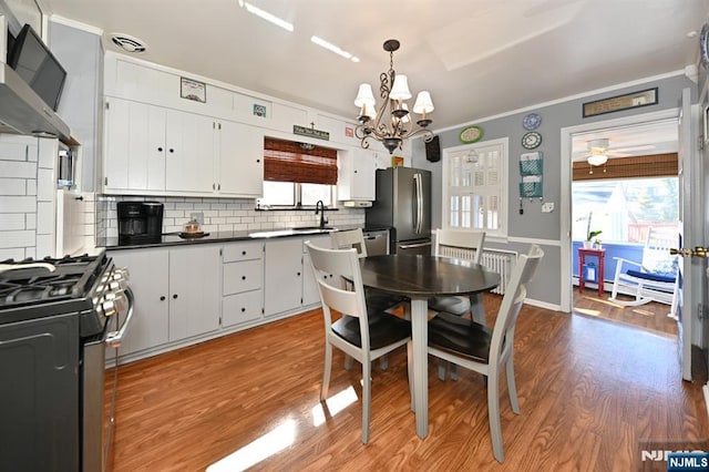 kitchen featuring stainless steel appliances, dark countertops, white cabinetry, light wood-type flooring, and extractor fan