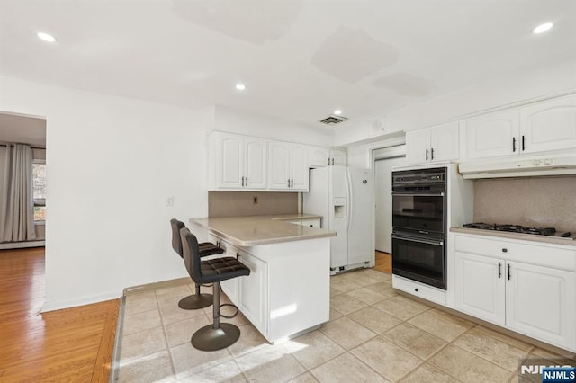 kitchen with white refrigerator with ice dispenser, double oven, a kitchen breakfast bar, white cabinets, and kitchen peninsula