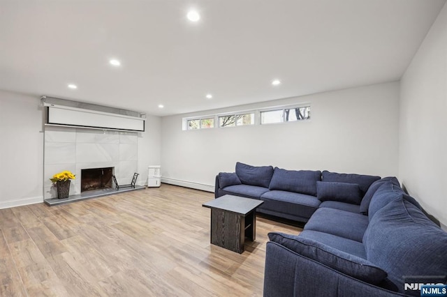 living room featuring light hardwood / wood-style floors, a tiled fireplace, and a baseboard radiator