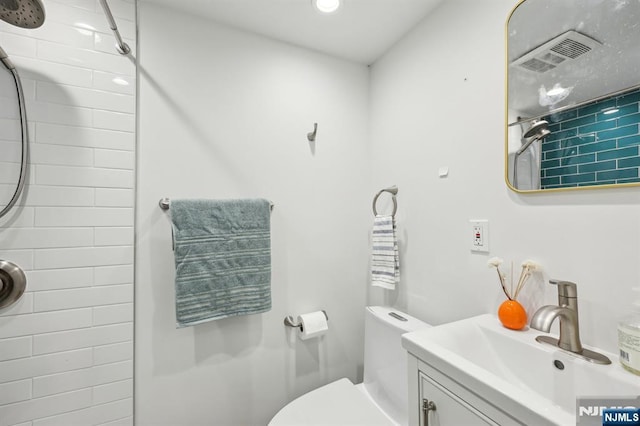 bathroom with toilet, a tile shower, and vanity