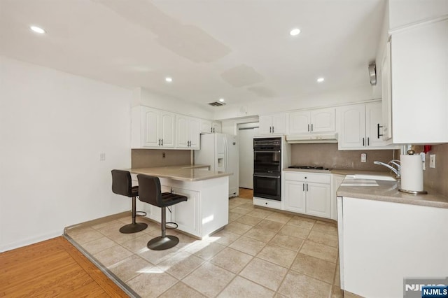 kitchen featuring a breakfast bar area, black double oven, white cabinets, gas stovetop, and white fridge with ice dispenser