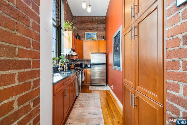 kitchen with appliances with stainless steel finishes, sink, light wood-type flooring, decorative light fixtures, and brick wall