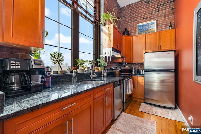 kitchen with dark stone countertops, light hardwood / wood-style flooring, sink, stainless steel appliances, and tasteful backsplash