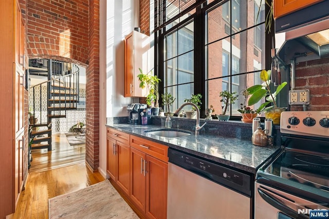 bar featuring light hardwood / wood-style floors, stainless steel appliances, dark stone counters, and sink