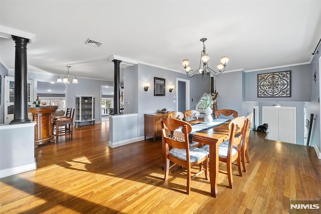 dining area featuring wood finished floors, visible vents, ornate columns, and an inviting chandelier