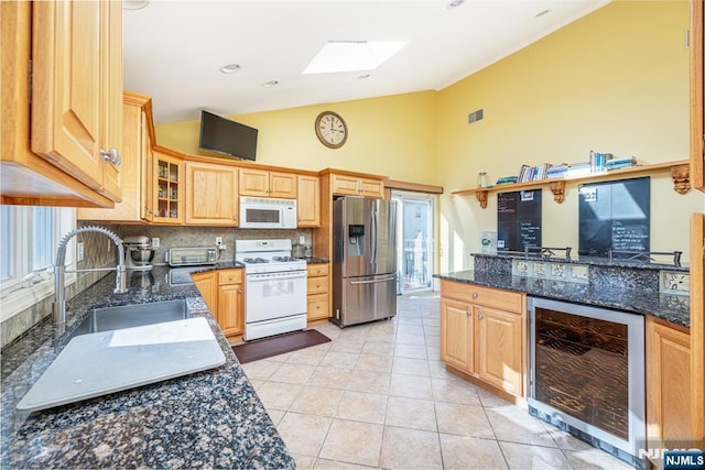 kitchen with white appliances, beverage cooler, light tile patterned flooring, dark stone counters, and a skylight