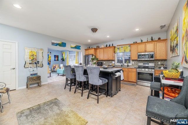 kitchen with appliances with stainless steel finishes, a breakfast bar, backsplash, a center island, and plenty of natural light