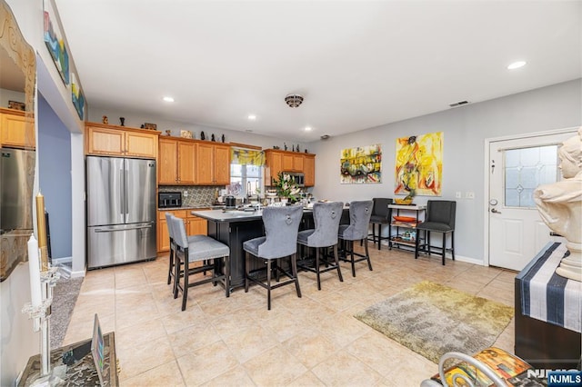 kitchen with a center island with sink, appliances with stainless steel finishes, a breakfast bar, light tile patterned floors, and tasteful backsplash