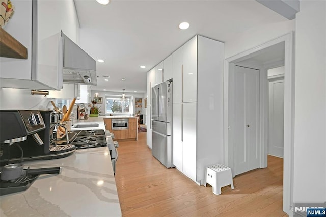 kitchen featuring light stone countertops, freestanding refrigerator, white cabinetry, modern cabinets, and wall chimney exhaust hood