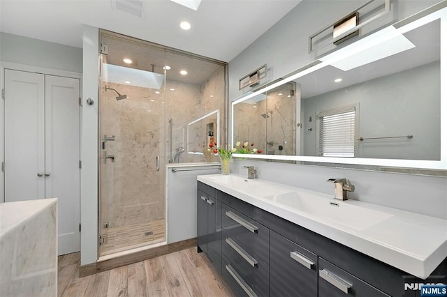 full bathroom featuring a skylight, double vanity, visible vents, a sink, and wood finished floors