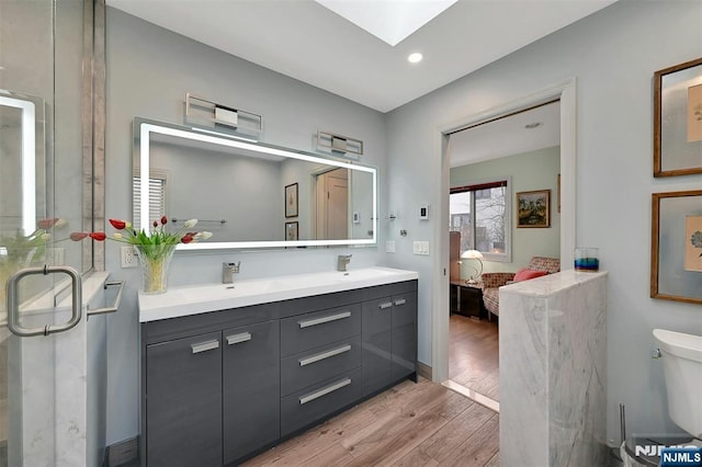 ensuite bathroom featuring a skylight, ensuite bath, a sink, and wood finished floors