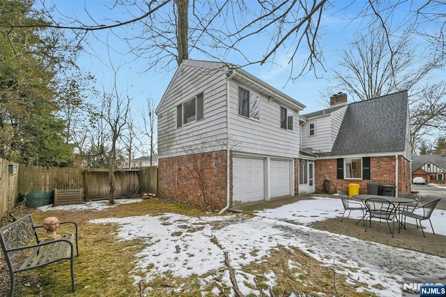 exterior space with a garage, brick siding, a chimney, and fence