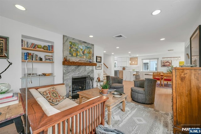 living room with a large fireplace, built in features, visible vents, wood finished floors, and recessed lighting