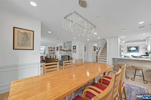 dining area featuring a wainscoted wall, recessed lighting, visible vents, stairway, and a large fireplace