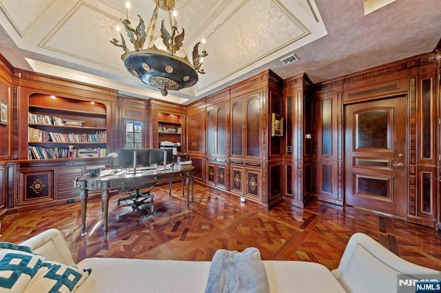 home office with dark parquet floors, ornamental molding, a raised ceiling, built in features, and a chandelier