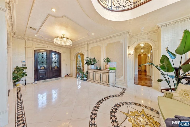 entryway featuring french doors, a tray ceiling, a chandelier, and ornamental molding