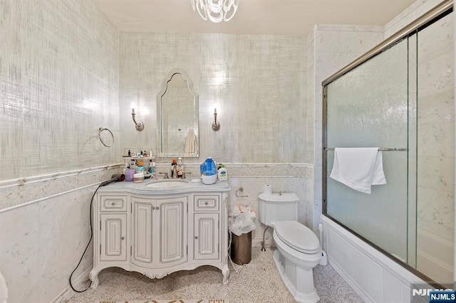 full bathroom with tile walls, shower / bath combination with glass door, vanity, and toilet