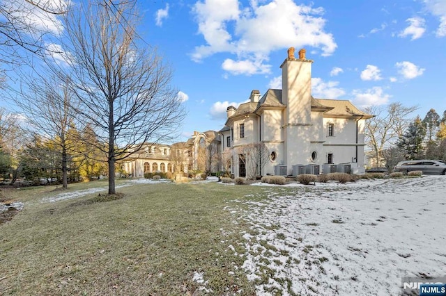 snow covered rear of property featuring cooling unit and a lawn