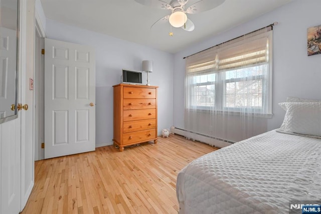 bedroom with a baseboard heating unit, light wood-type flooring, and a ceiling fan