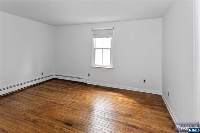 spare room featuring a baseboard heating unit and dark hardwood / wood-style floors