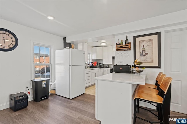 kitchen with kitchen peninsula, light hardwood / wood-style floors, white fridge, white cabinets, and a kitchen breakfast bar