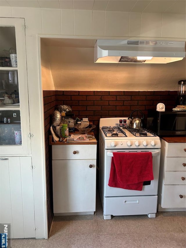 kitchen with under cabinet range hood, brick wall, white cabinetry, and gas range gas stove