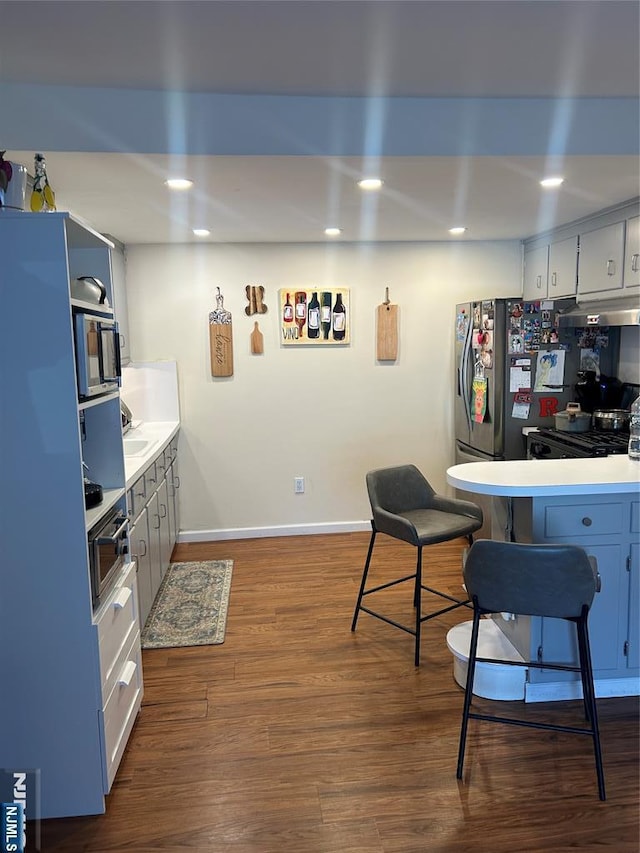 kitchen with a breakfast bar area, appliances with stainless steel finishes, dark wood-type flooring, light countertops, and under cabinet range hood