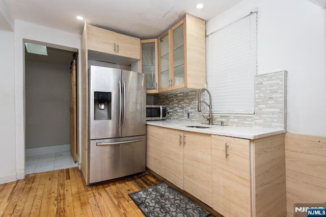 kitchen with tasteful backsplash, stainless steel appliances, light brown cabinets, sink, and light wood-type flooring