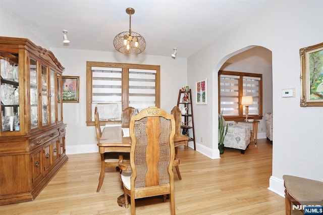 dining space with arched walkways, light wood finished floors, an inviting chandelier, and baseboards