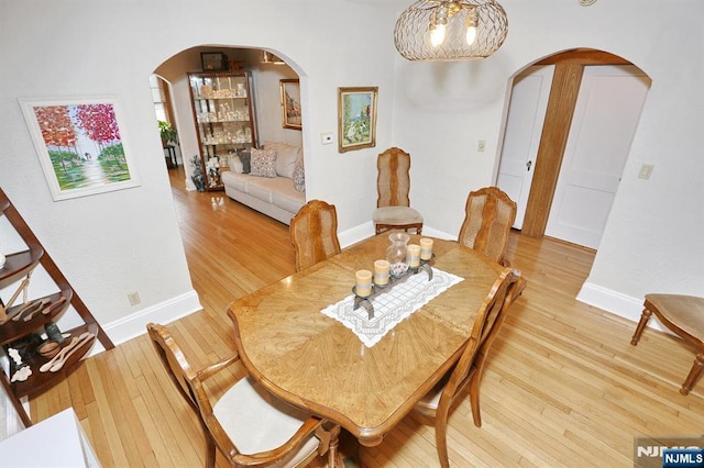 dining space with arched walkways, baseboards, and light wood-style floors