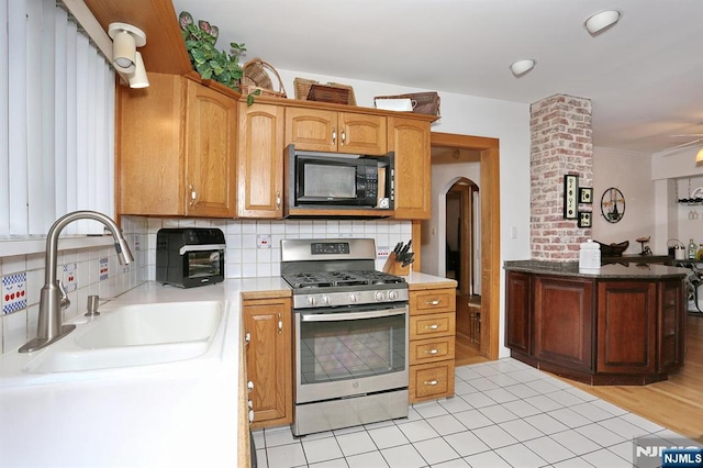 kitchen featuring a sink, light countertops, black microwave, backsplash, and gas stove