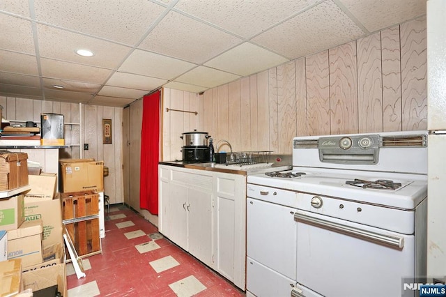 kitchen with a paneled ceiling, light floors, white range with gas stovetop, and white cabinetry