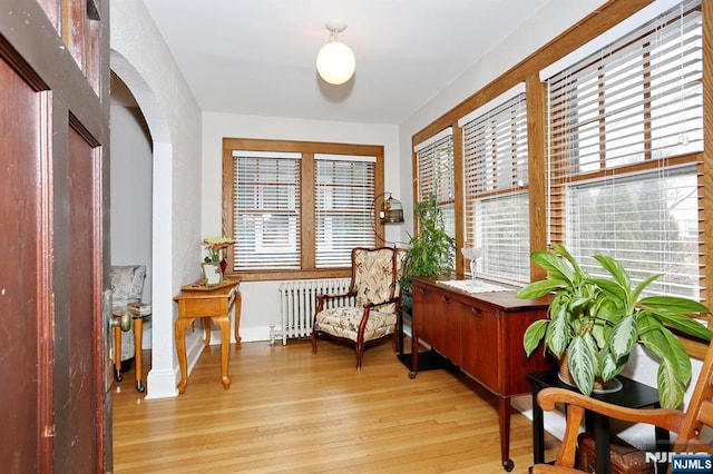 sitting room featuring arched walkways, radiator heating unit, and light wood-type flooring