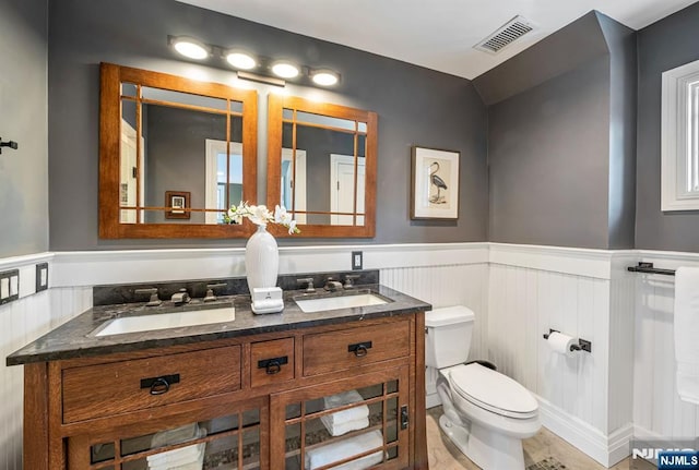 bathroom with a wainscoted wall, toilet, a sink, and visible vents