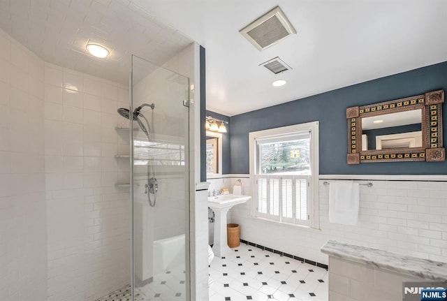 bathroom with a wainscoted wall, a shower stall, and visible vents