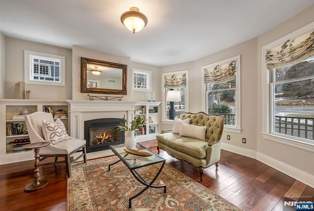 living area with baseboards, dark wood-style flooring, a fireplace with flush hearth, and a healthy amount of sunlight