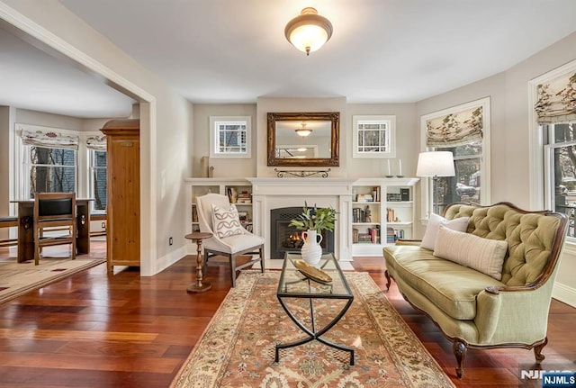 living area with a warm lit fireplace, dark wood finished floors, and baseboards