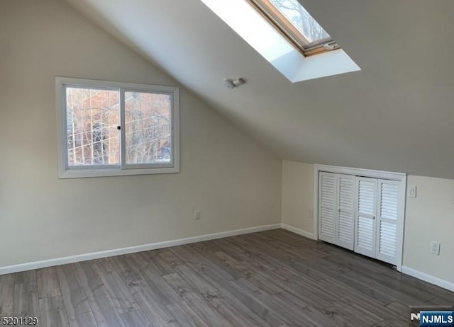 additional living space with vaulted ceiling with skylight and dark hardwood / wood-style floors