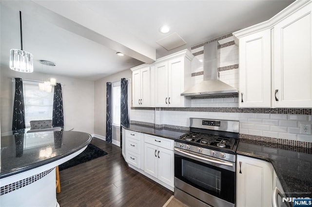 kitchen with decorative light fixtures, wall chimney range hood, dark wood-type flooring, white cabinets, and gas range