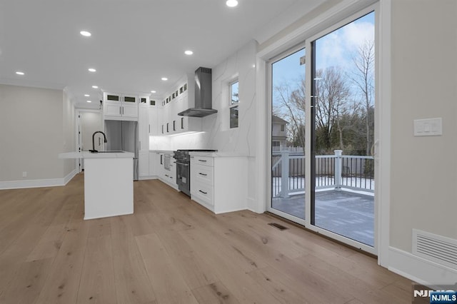 kitchen featuring wall chimney exhaust hood, white cabinets, high end stainless steel range, sink, and a kitchen island with sink