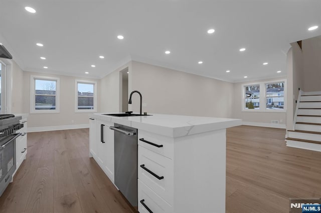 kitchen with light stone countertops, white cabinets, ornamental molding, sink, and a kitchen island with sink