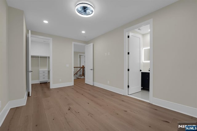 unfurnished bedroom featuring connected bathroom, a walk in closet, and light hardwood / wood-style floors