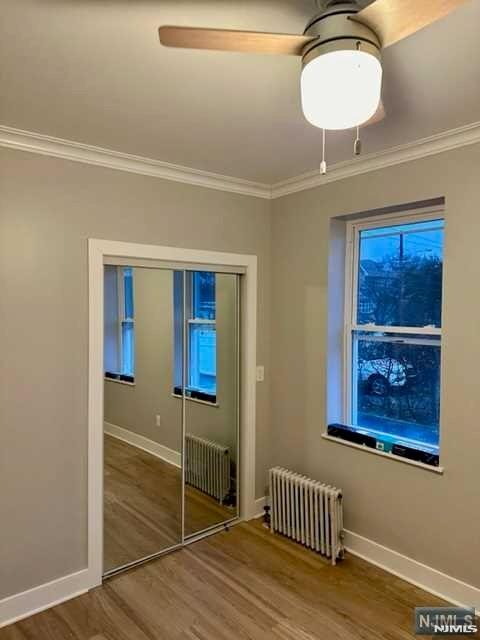 unfurnished bedroom with baseboards, radiator, wood finished floors, and ornamental molding